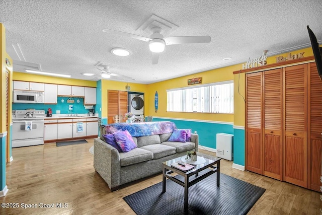 living room with stacked washer / dryer, ceiling fan, sink, and light wood-type flooring