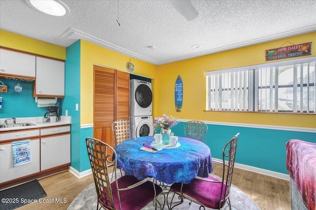 dining area with sink, light wood-type flooring, a textured ceiling, and stacked washer / dryer