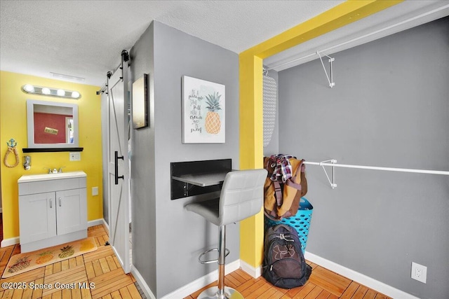 interior space with a barn door, light hardwood / wood-style floors, sink, and a textured ceiling