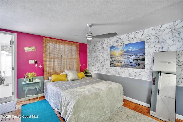 bedroom featuring ceiling fan, hardwood / wood-style flooring, a barn door, and a textured ceiling