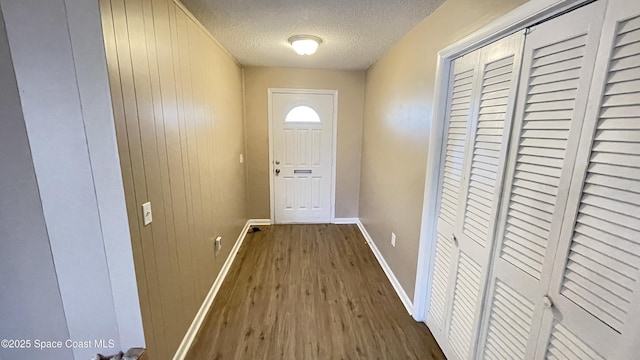 doorway featuring a textured ceiling, dark wood-type flooring, wood walls, and baseboards