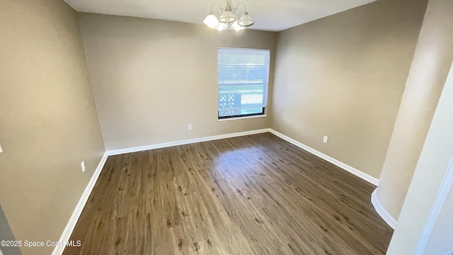 spare room featuring an inviting chandelier, wood finished floors, and baseboards