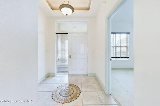 foyer entrance featuring light tile patterned floors, baseboards, and a raised ceiling