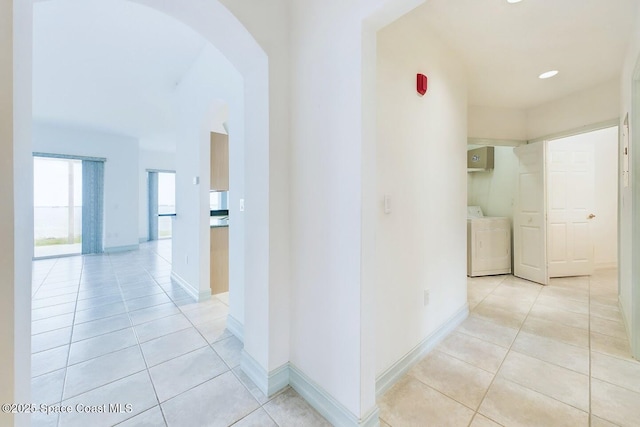 hallway with light tile patterned floors, baseboards, arched walkways, washer and dryer, and recessed lighting