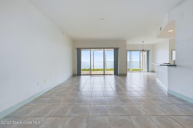 unfurnished room with light tile patterned flooring, baseboards, and an inviting chandelier