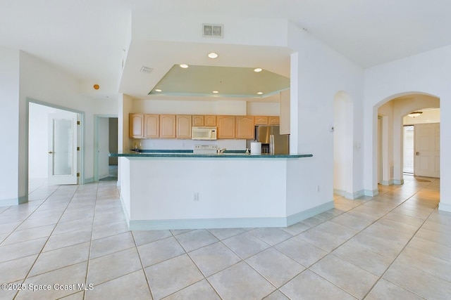 kitchen with dark countertops, white microwave, light brown cabinets, a peninsula, and stainless steel fridge with ice dispenser