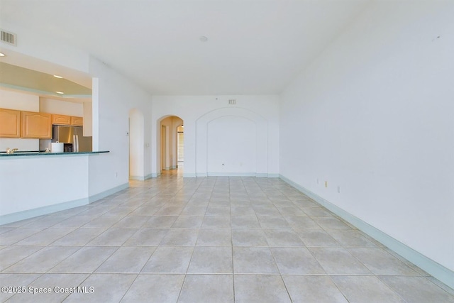 unfurnished living room featuring arched walkways, light tile patterned floors, visible vents, and baseboards