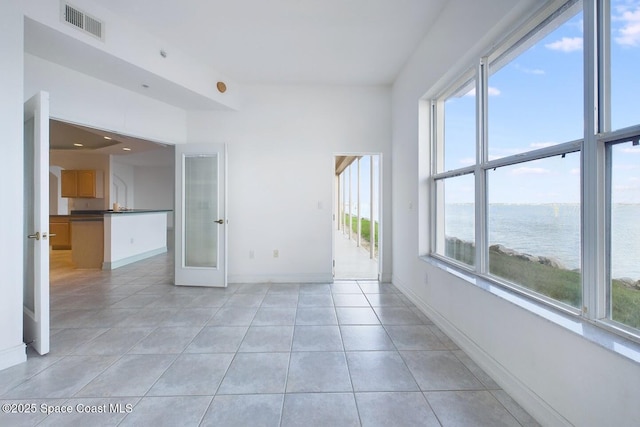 empty room with light tile patterned floors, a water view, visible vents, baseboards, and french doors