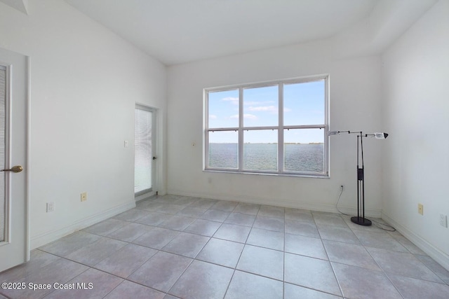 spare room with a water view, light tile patterned flooring, and baseboards