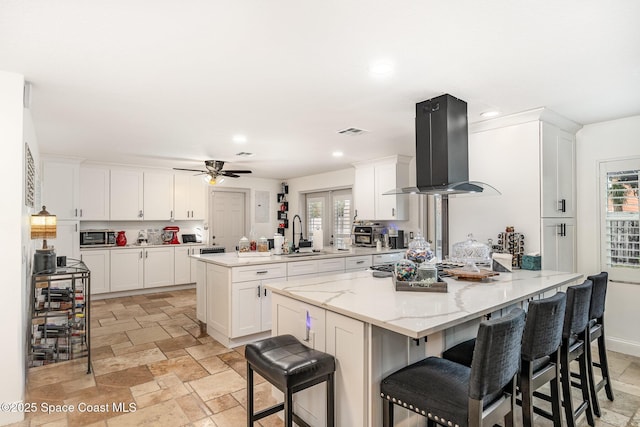230 Andros Dr, Merritt Island, FL 32952 - kitchen with light stone counters, white cabinetry, island range hood, a center island with sink, and a kitchen breakfast bar