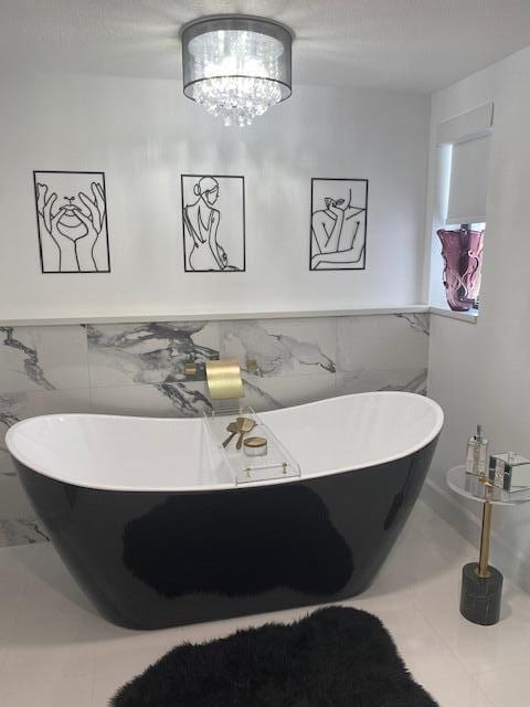 bathroom with a bathing tub, tile walls, and a notable chandelier