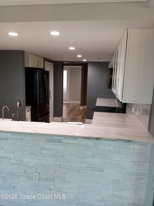 kitchen with sink, black fridge with ice dispenser, kitchen peninsula, and white cabinets