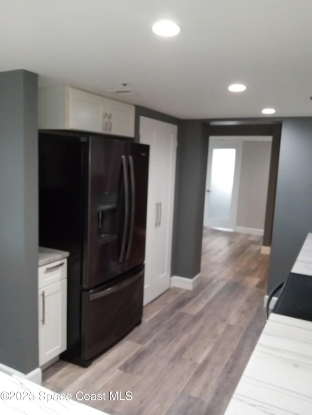 kitchen with white cabinets, black fridge with ice dispenser, and light hardwood / wood-style floors