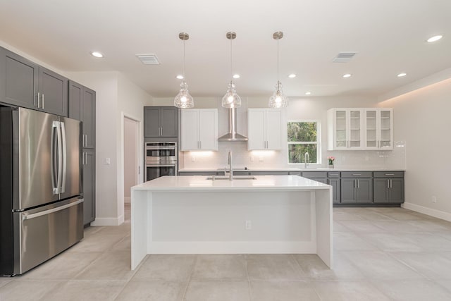 kitchen with appliances with stainless steel finishes, gray cabinetry, a kitchen island with sink, white cabinets, and decorative light fixtures