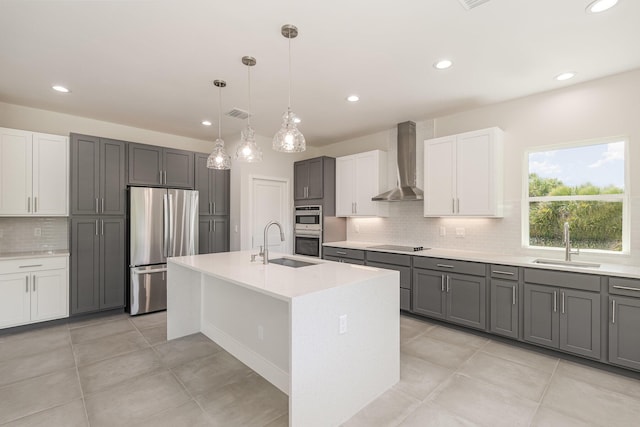 kitchen with white cabinetry, an island with sink, sink, stainless steel appliances, and wall chimney exhaust hood