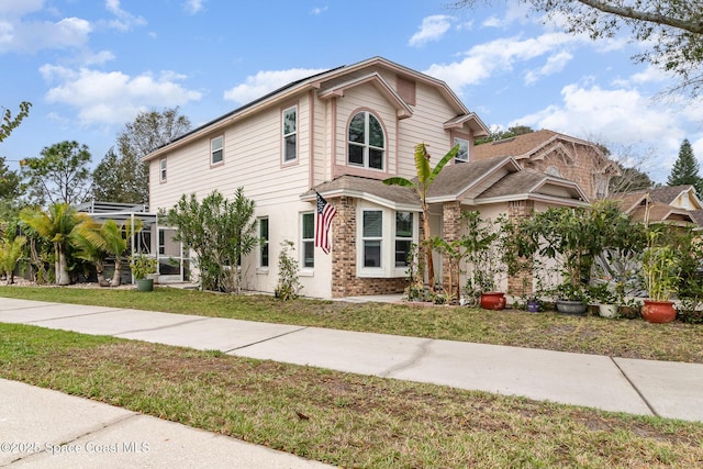 view of front facade featuring brick siding, a front yard, and a lanai