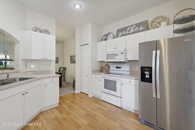 kitchen with white cabinetry, a sink, light countertops, light wood-style floors, and white appliances