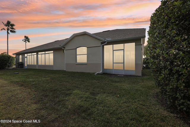 rear view of property with stucco siding, a lawn, and roof with shingles