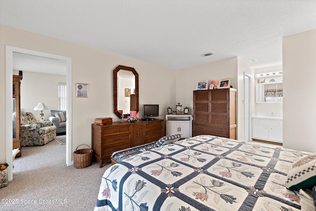 bedroom featuring visible vents, ensuite bathroom, a textured ceiling, and light colored carpet