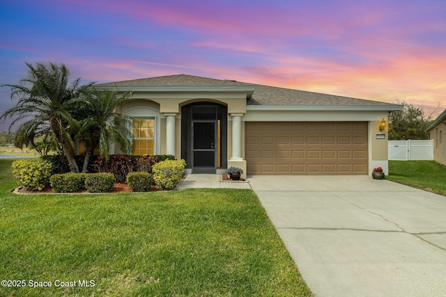 view of front of house with a garage, a lawn, fence, and stucco siding