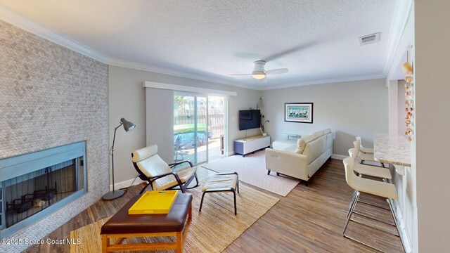 living area with a tiled fireplace, wood finished floors, visible vents, and ornamental molding