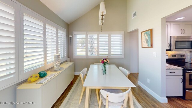 dining room featuring baseboards, lofted ceiling, visible vents, and wood finished floors