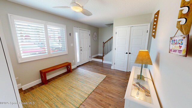 foyer with stairway, a ceiling fan, baseboards, and wood finished floors