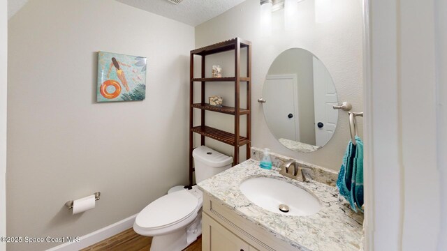 bathroom with vanity, wood finished floors, baseboards, a textured ceiling, and toilet