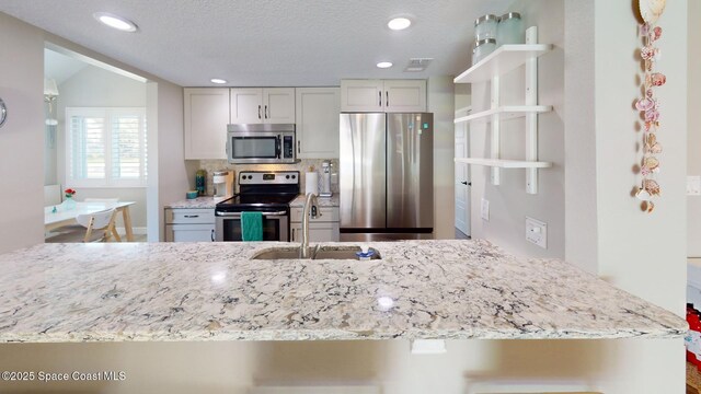 kitchen featuring visible vents, backsplash, light stone counters, stainless steel appliances, and a sink