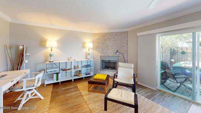 living area with a textured ceiling, wood finished floors, a fireplace, and ornamental molding