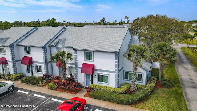 view of front of property featuring stucco siding, uncovered parking, and a shingled roof