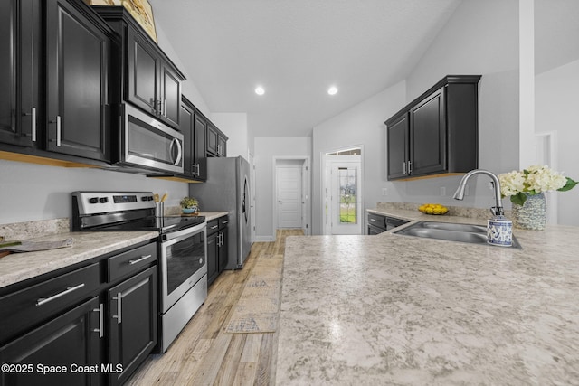 kitchen featuring vaulted ceiling, appliances with stainless steel finishes, sink, and light hardwood / wood-style flooring