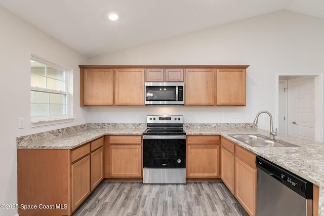 kitchen featuring sink, vaulted ceiling, appliances with stainless steel finishes, kitchen peninsula, and light hardwood / wood-style floors