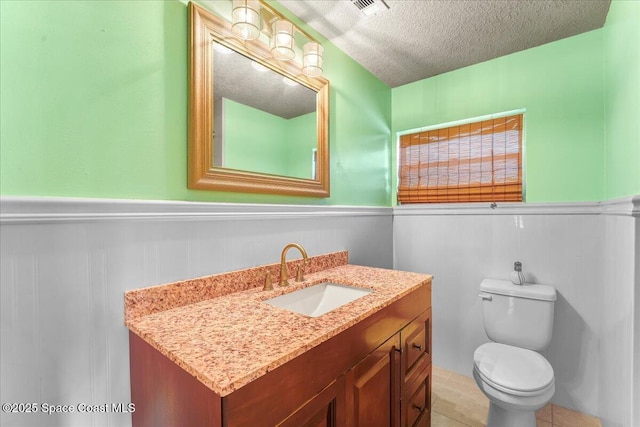 half bathroom featuring a textured ceiling, wainscoting, vanity, and toilet