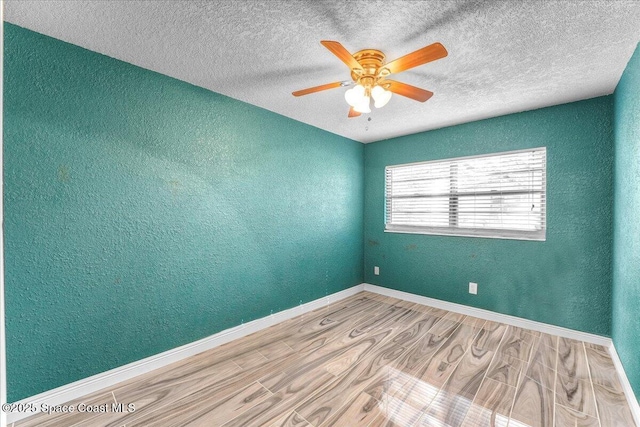 empty room with a textured wall, ceiling fan, baseboards, and wood finished floors