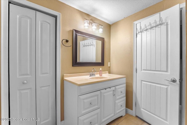 bathroom with a textured ceiling, a textured wall, tile patterned flooring, vanity, and a closet