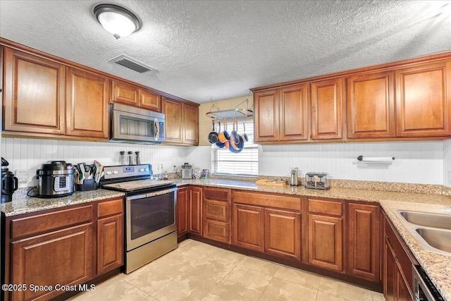 kitchen featuring stainless steel appliances, brown cabinetry, visible vents, and light stone counters