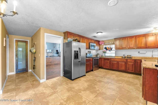 kitchen with visible vents, appliances with stainless steel finishes, brown cabinets, light stone counters, and a sink