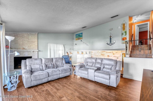 living area with a textured ceiling, a fireplace, wood finished floors, and visible vents