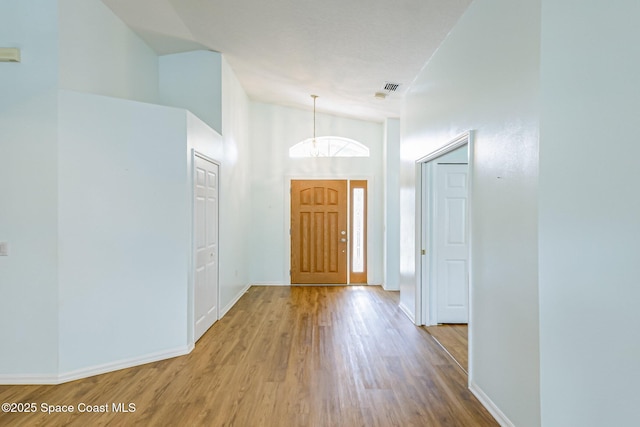 foyer entrance featuring lofted ceiling, visible vents, baseboards, and wood finished floors