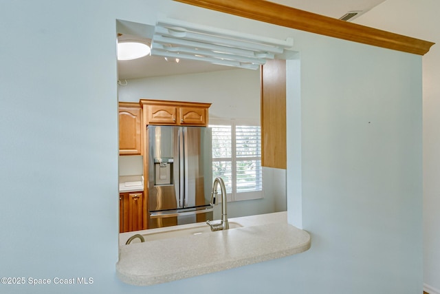 kitchen featuring stainless steel fridge, vaulted ceiling, light countertops, and a sink