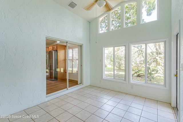 empty room featuring light tile patterned floors, visible vents, a textured wall, a ceiling fan, and high vaulted ceiling