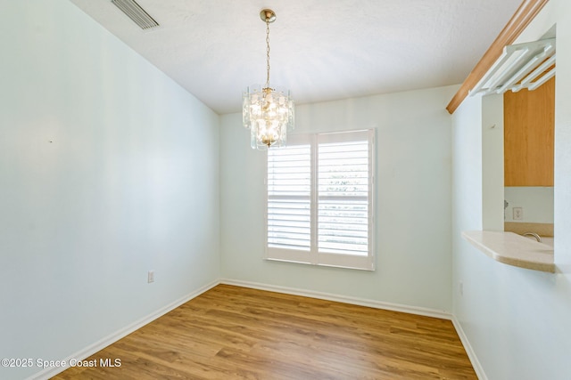 unfurnished dining area with a notable chandelier, visible vents, baseboards, and wood finished floors