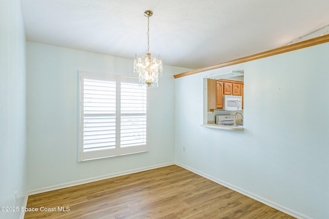 spare room featuring baseboards, wood finished floors, and a notable chandelier