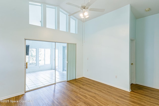 spare room with high vaulted ceiling, ceiling fan, baseboards, and wood finished floors