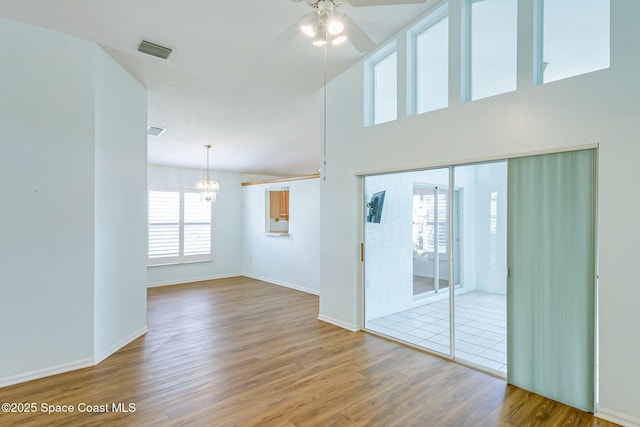 spare room with ceiling fan with notable chandelier, a high ceiling, wood finished floors, visible vents, and baseboards