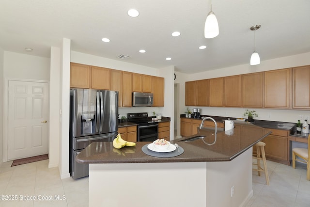 kitchen with appliances with stainless steel finishes, dark countertops, a center island with sink, and hanging light fixtures