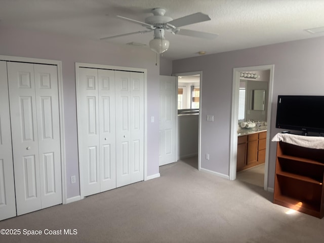 bedroom featuring two closets, light colored carpet, a ceiling fan, ensuite bath, and baseboards