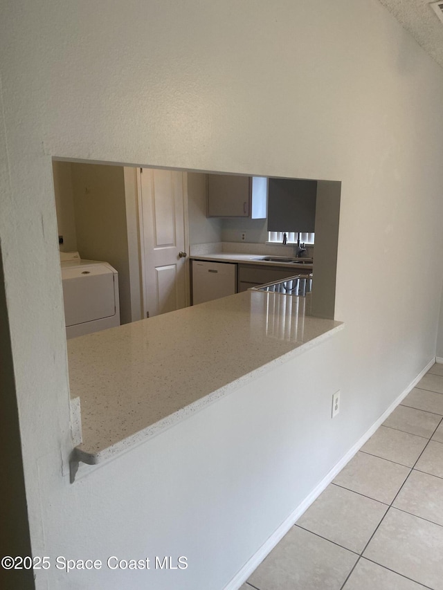 kitchen featuring dishwasher, light stone counters, washer / dryer, light tile patterned floors, and kitchen peninsula