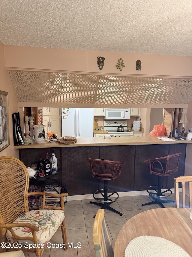 interior space featuring white appliances, light tile patterned floors, a breakfast bar area, and a textured ceiling